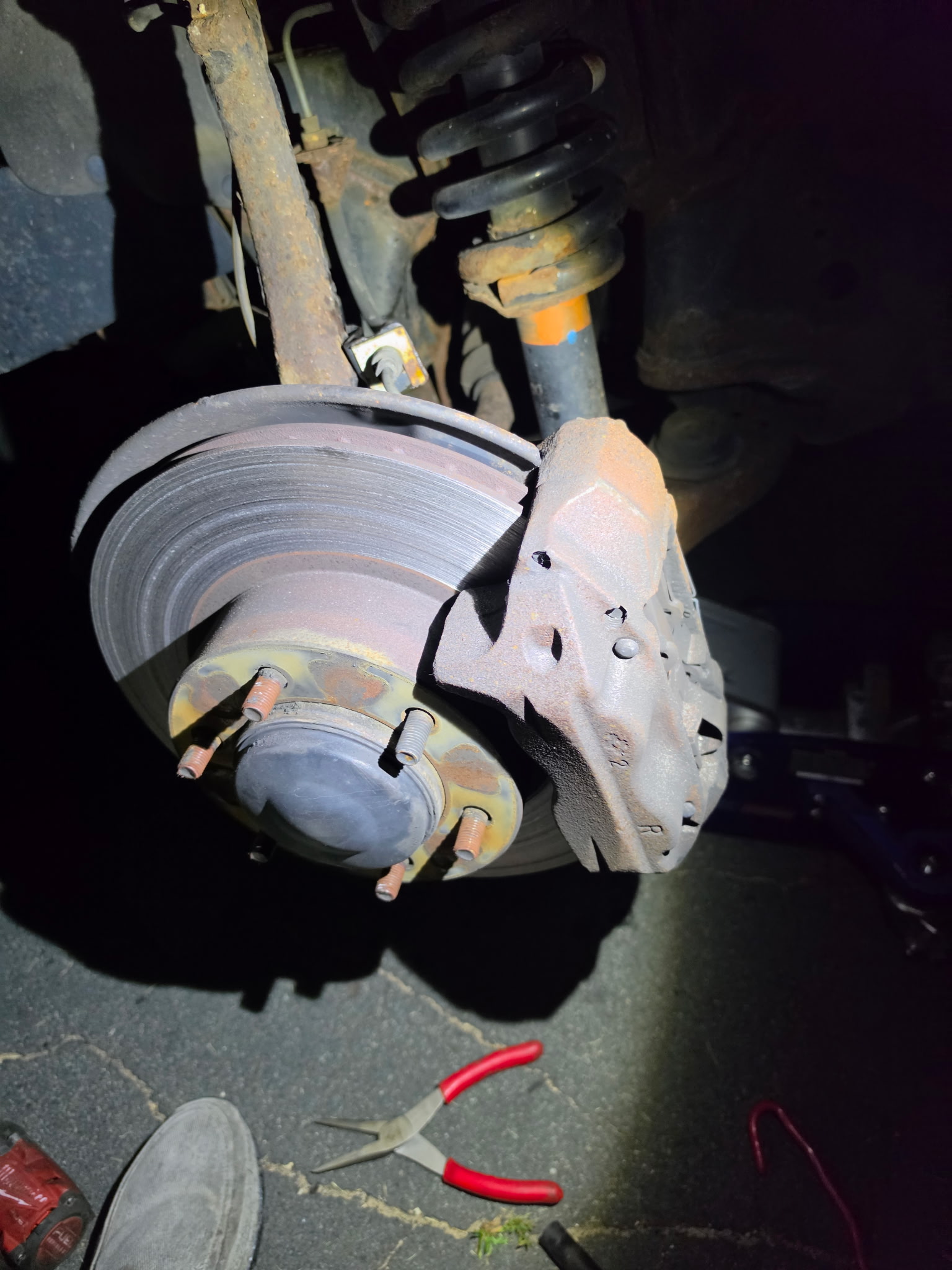 New brake pads in caliper next to worn rotor during on-site brake pad and rotor replacement