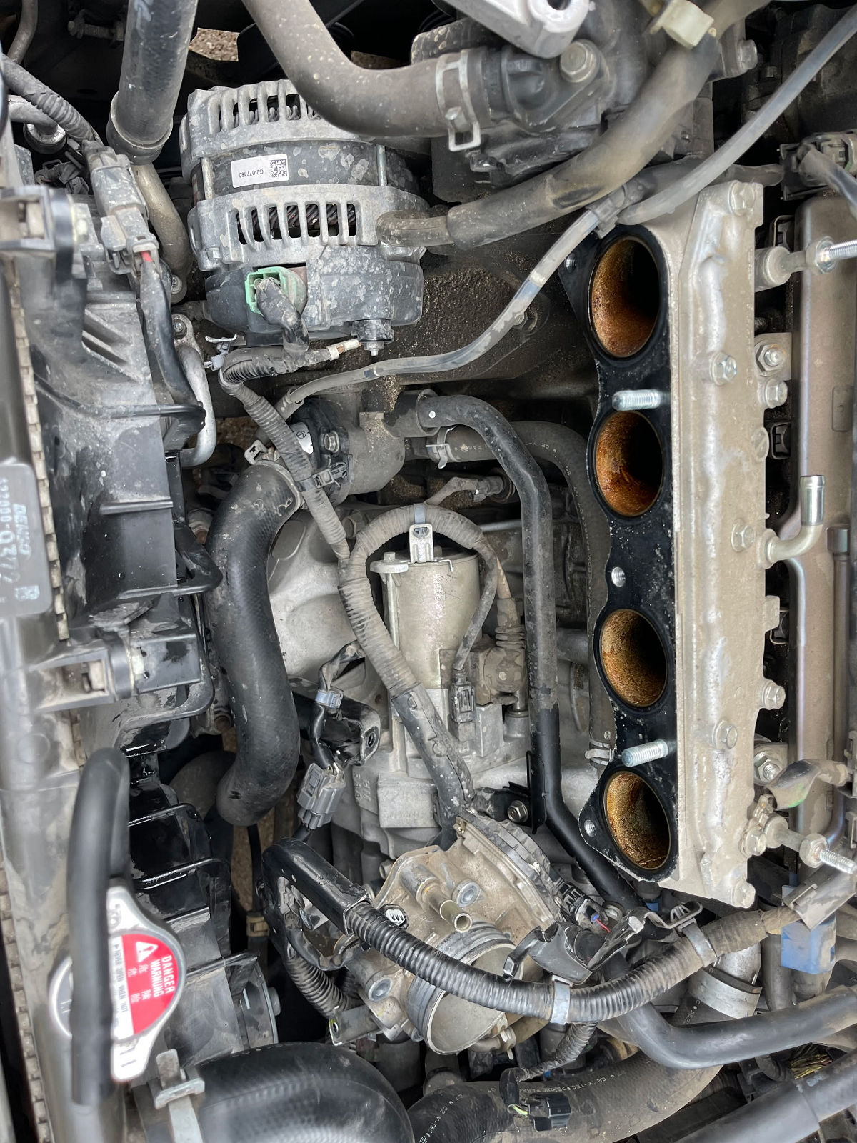 Four-cylinder engine bay showing intake manifold, alternator, and serpentine belt during a mobile mechanic engine inspection
