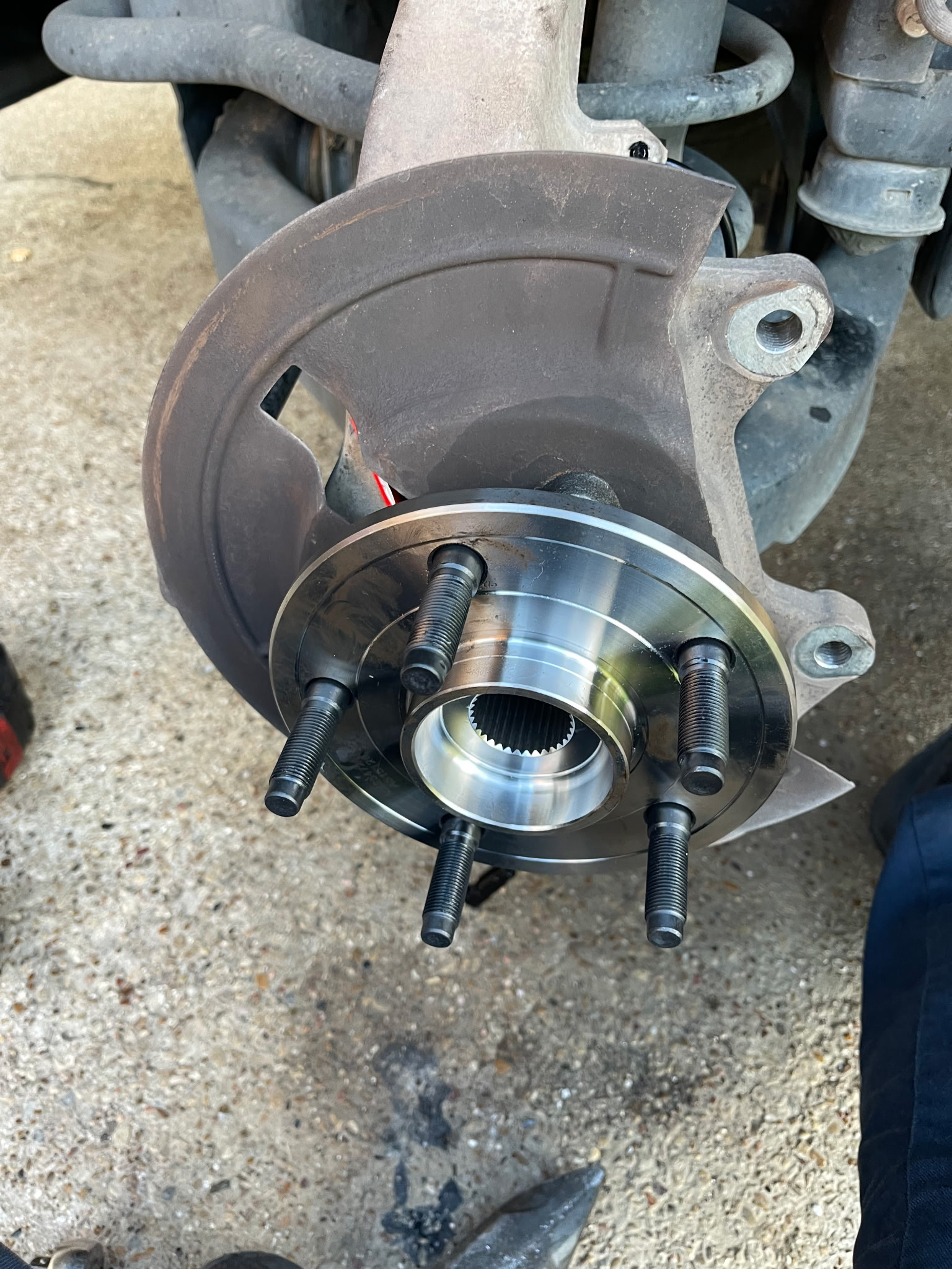 A freshly installed wheel hub assembly with a polished spindle and new bearing is being mounted to a vehicle's suspension
